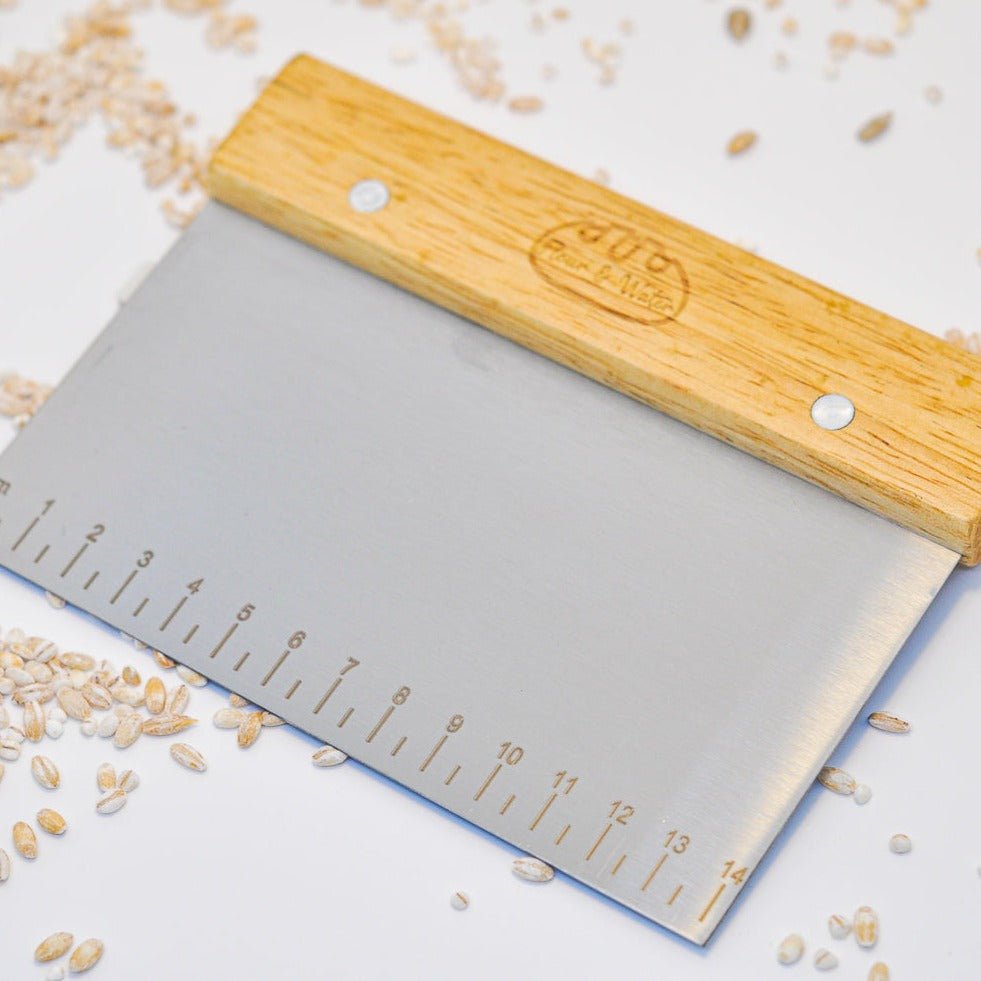 Close-up of the bench scraper blade and oak handle among scattered grains