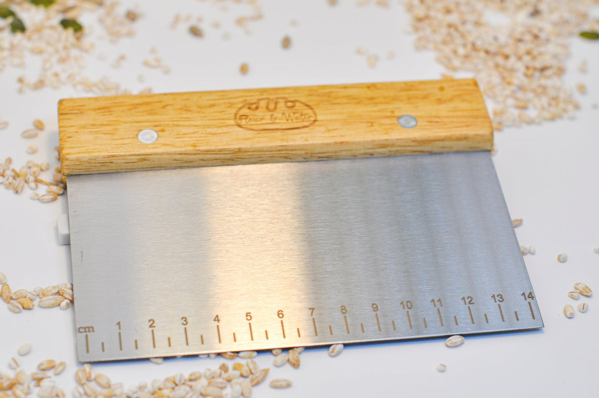 Stainless steel bench scraper with oak handle on a white bench