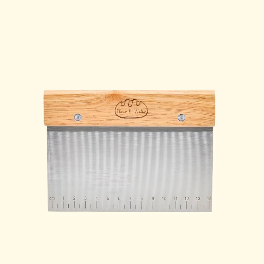 Bench scraper with oak handle and engraved logo on a cream background