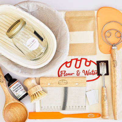 Ultimate Sourdough Baker Set flat lay: bannetons, starter jar, dough whisk, scrapers, lame, brush, oil and scoop