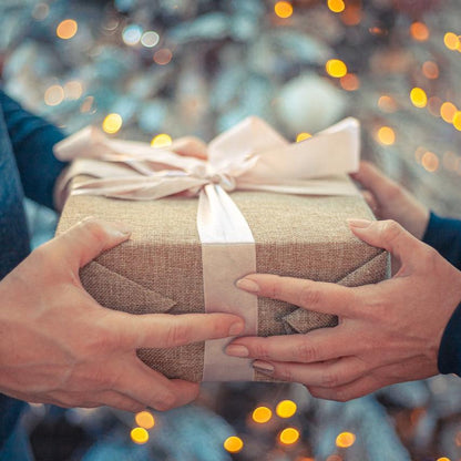 Hands passing a gift wrapped in brown paper and ribbon